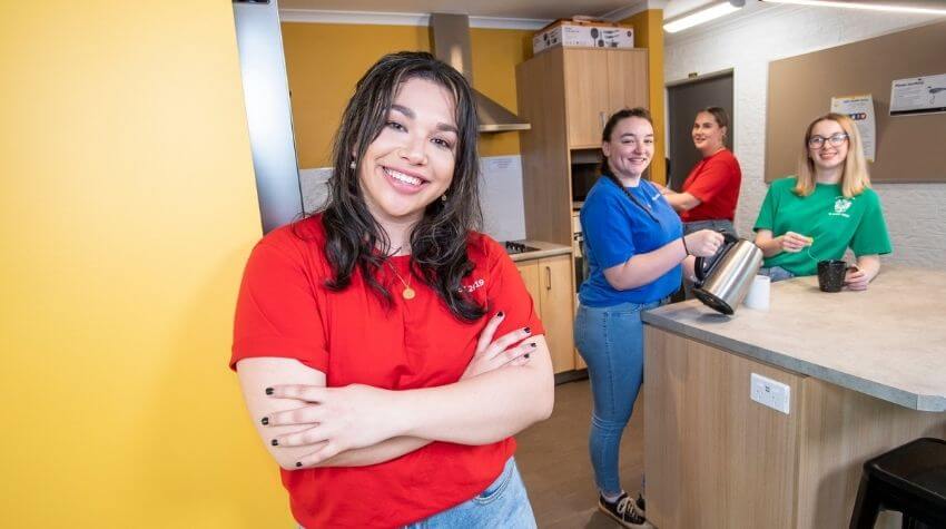 Group of cheerful coworkers in colorful uniforms inside a modern kitchen area.