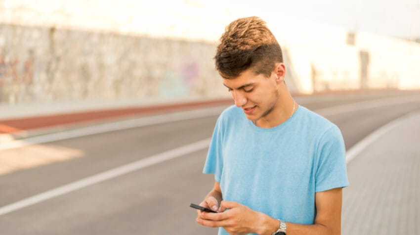 A teenager stands in a street on his phone.