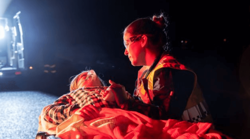 UniSQ alumni, Sally Jacobs, as a paramedic holding the hand of a patient