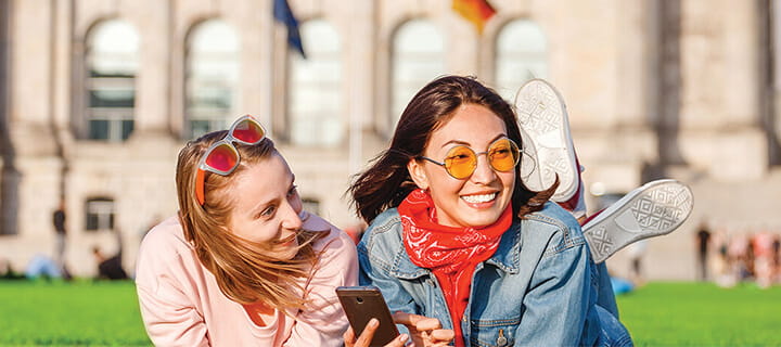 Two women taking a selfie, one with red sunglasses on her head, both smiling and posing playfully outdoors.
